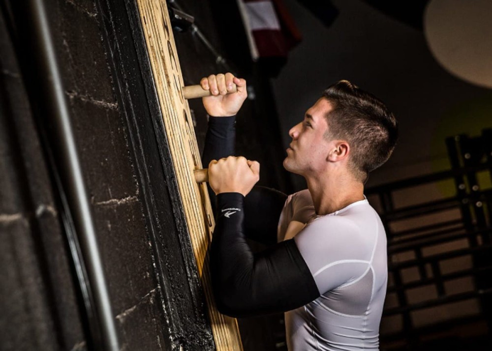 a man wearing compression sleeves and climbing a wall with pegs for a workout