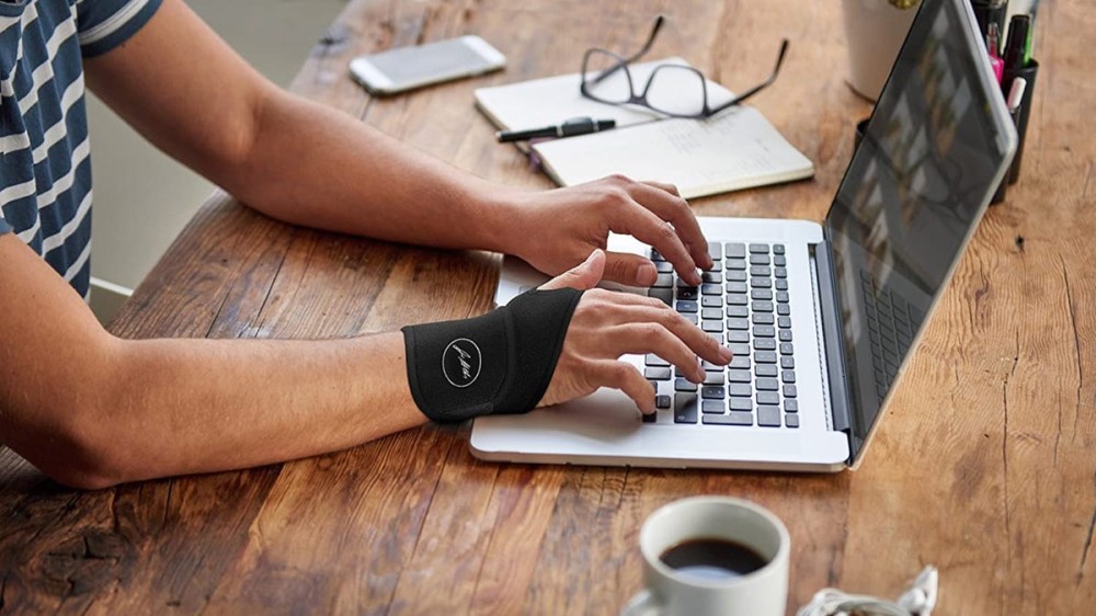 A person wears a black brace while typing on their laptop.