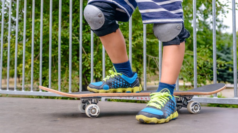 Young boy standing at the top of a ramp at the skate park with one foot on his skateboard, close up of his feet in colorful blue and yellow sneakers.