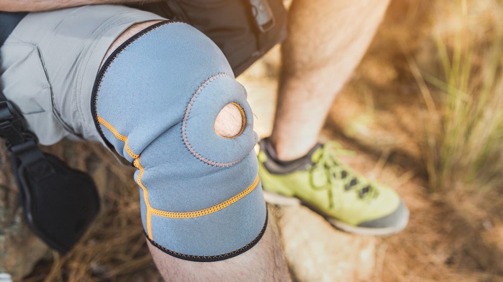 A man's knee in a blue knee brace while he rests on a hike.